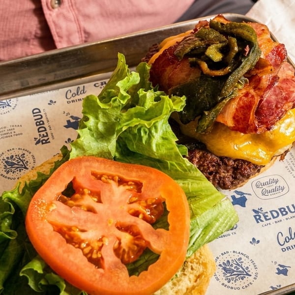 A Redbud Cafe burger with bacon, cheese, and grilled peppers, served open-faced with lettuce, tomato, and a pickle.